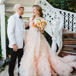 the couple stands side by side under the spiral staircase
