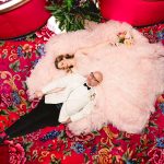 this is an aerial view of a couple laying on the pink floral carpet at madonna inn. the bride is wearing a fluffy pink dress and the groom is in a white tuxedo.