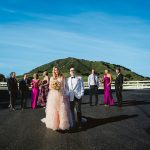 wedding party walks toward the photographer's camera. there is a beautiful blue sky and a green mossy hill in the background.