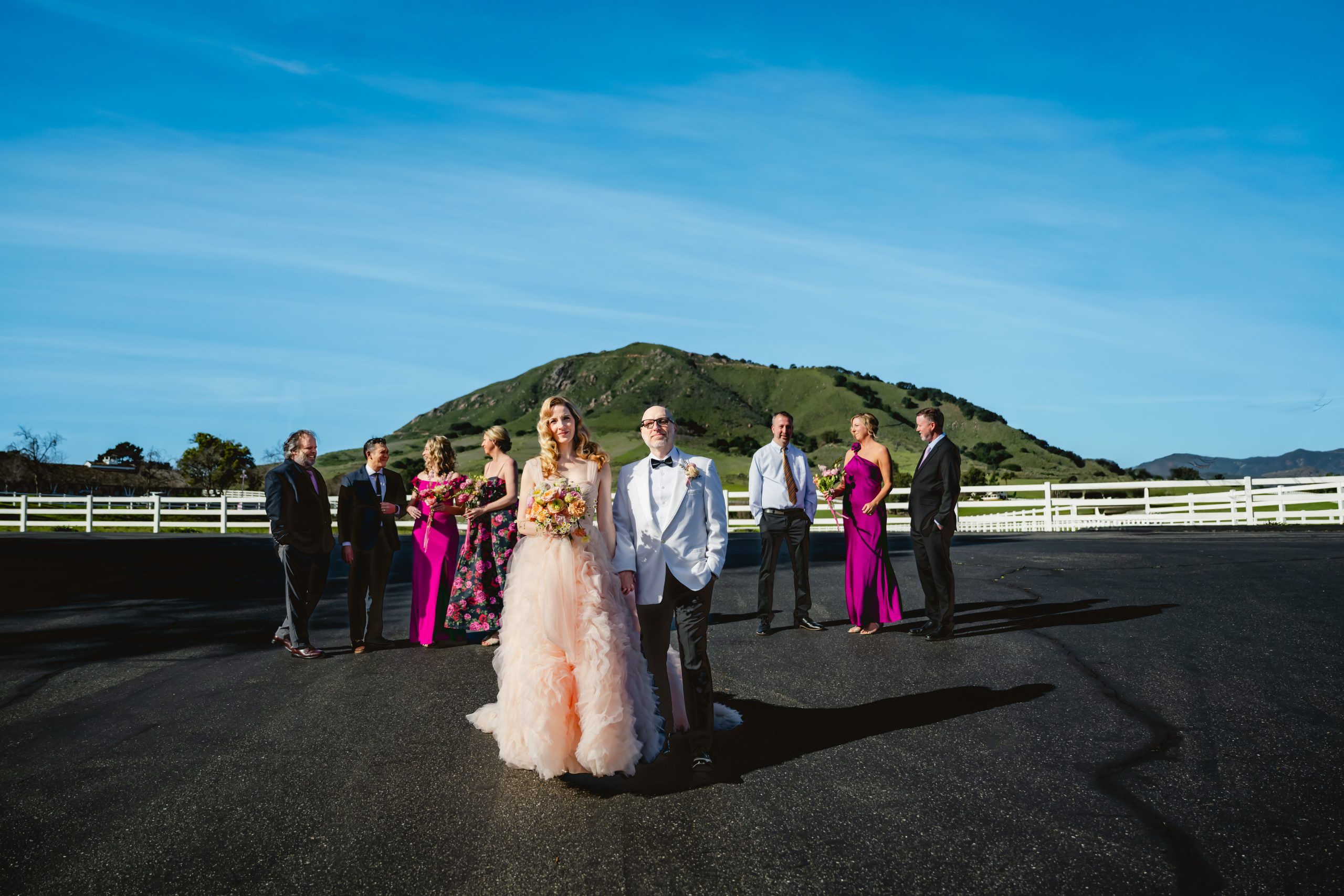 wedding party walks toward the photographer's camera. there is a beautiful blue sky and a green mossy hill in the background.