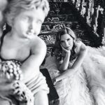 the bride sits with her head in her hand, gazing at the camera near a creepy cupid statue