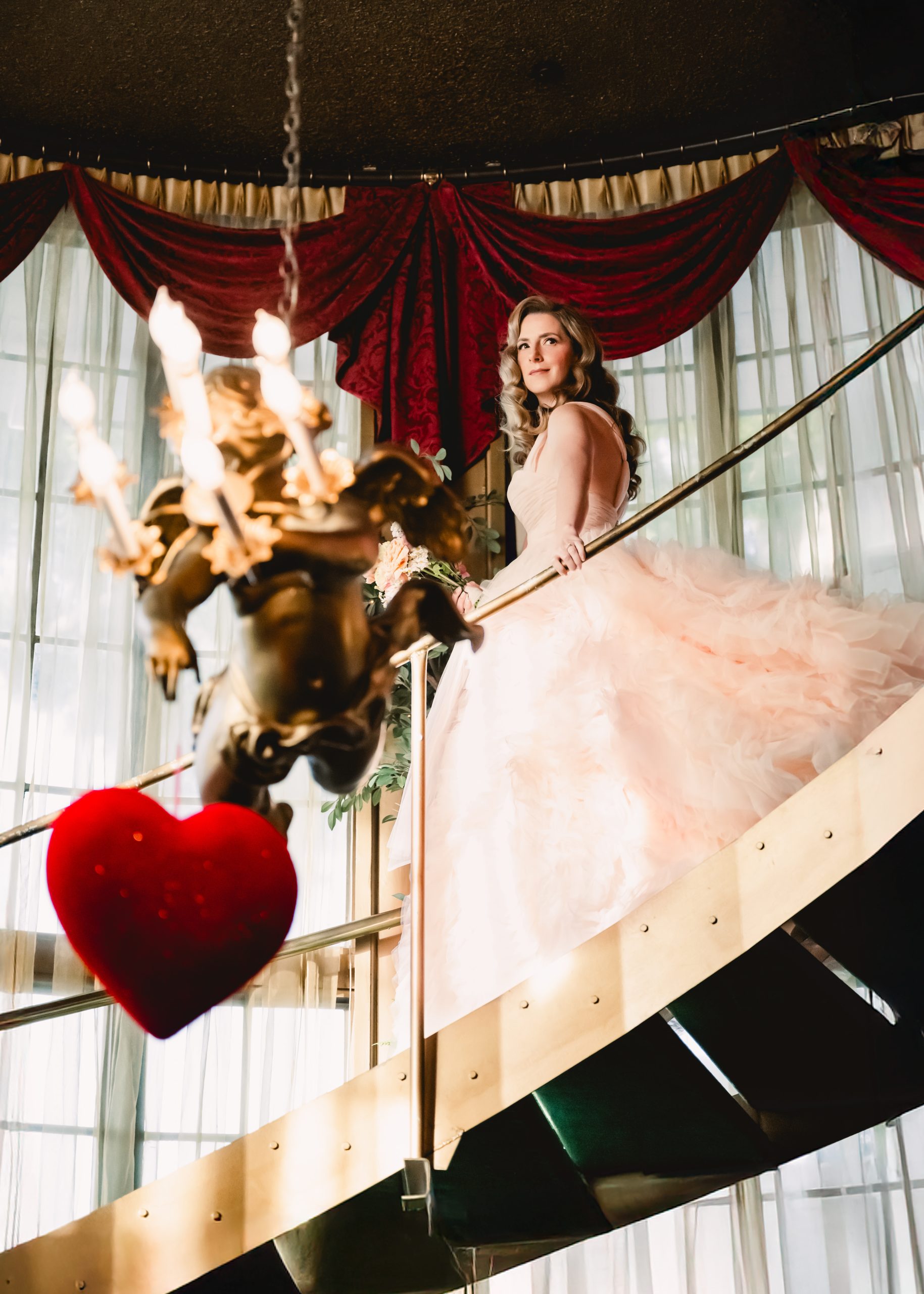 a bride in a fluffy pink wedding gown walks down the stairs into the ceremony