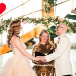 the bride and group gasp and laugh together as they hold hands under their floral arch