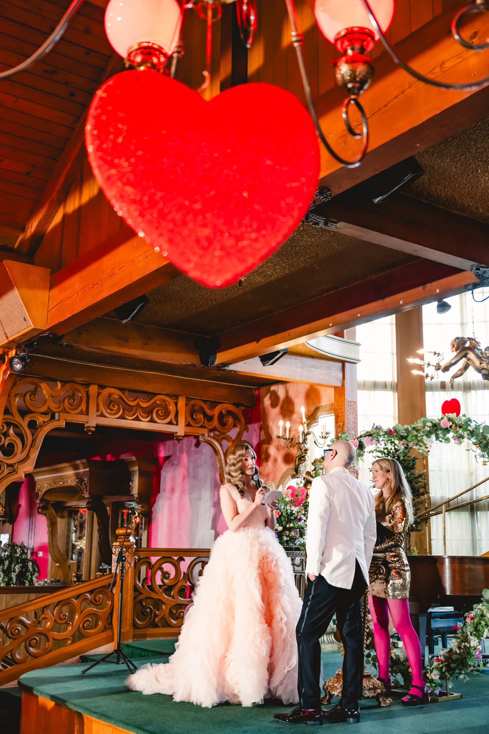 a blonde bridein a pink wedding gown reads her vows on stage at Madonna Inn