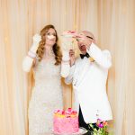 a bride in a vintage champagne mini dress and a groom in a white tuxedo laugh and flail around and feed each other their pink champagne cake as they cut it