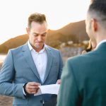 a groom in a light blue suit reads his vows to his husband
