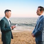 two grooms read their vows to each other heir elopement ceremony as the sun sets over the ocean in Malibu