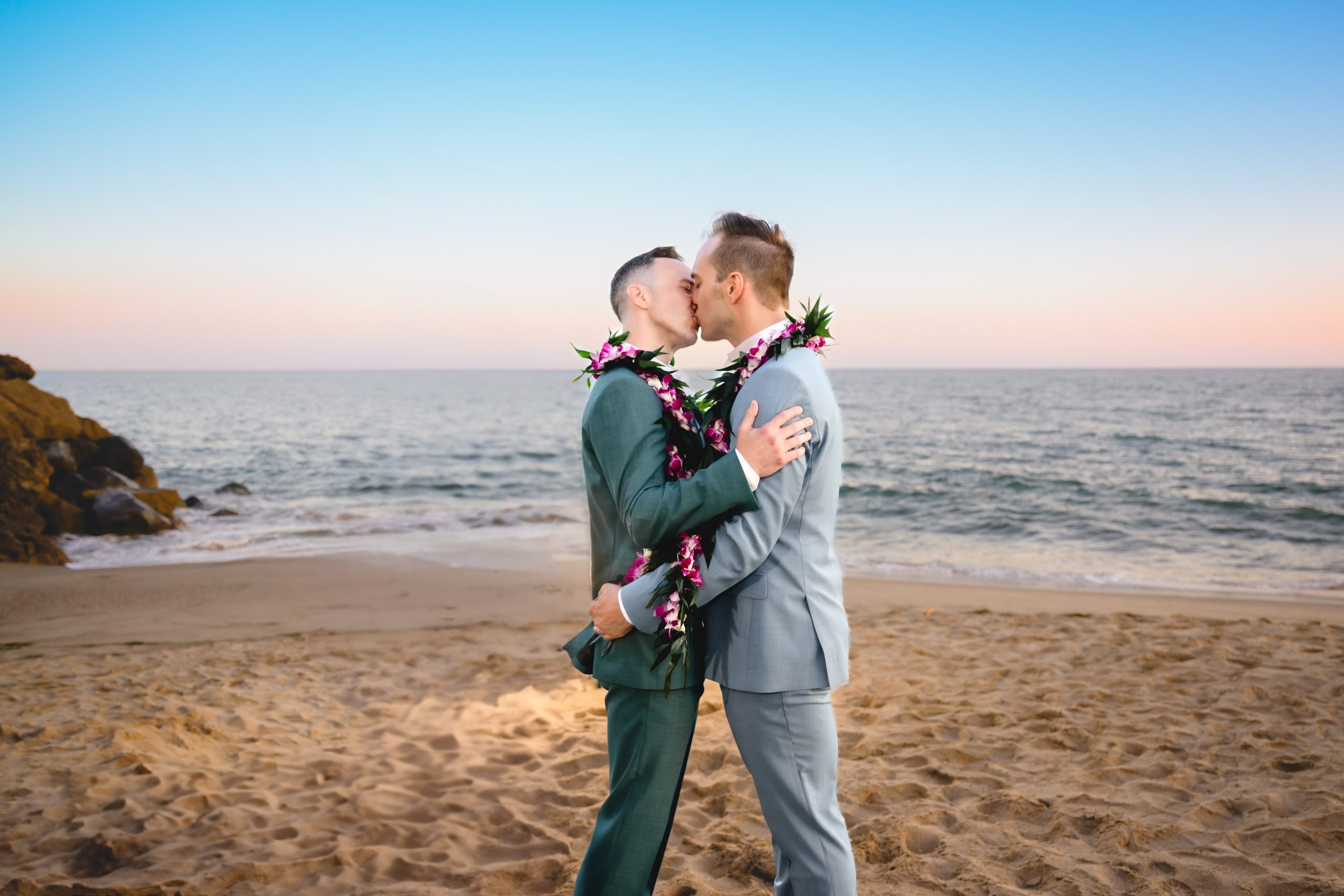 A couple embraces and have their first kiss as a married couple during their elopement ceremony on a malibu beach.  The sun is setting over the ocean behind them. 