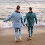 two grooms walk out towards the ocean on a malibu beach during sunset