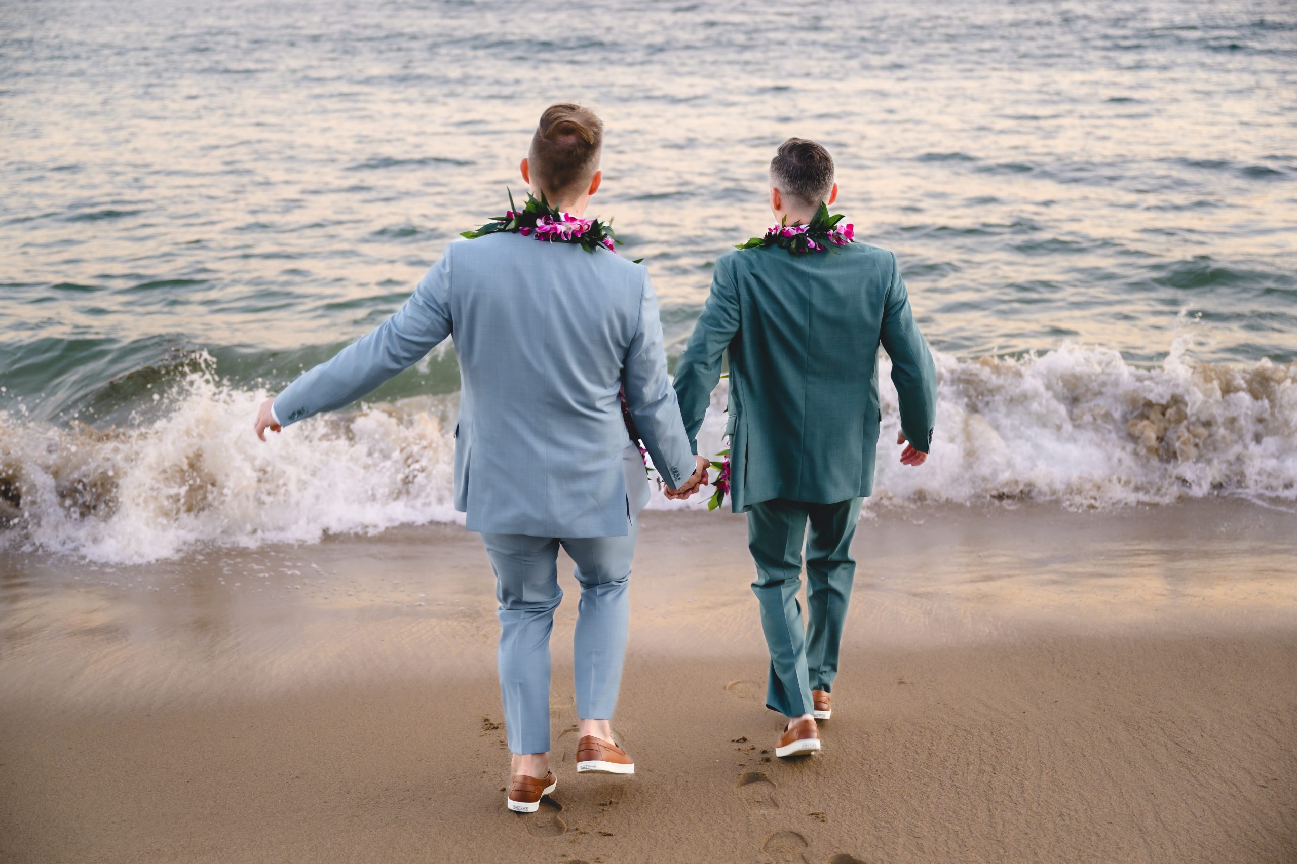 two grooms walk out towards the ocean on a malibu beach during sunset