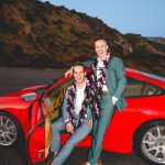 Two grooms pose in front of their red porsche on their wedding day