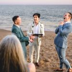 two grooms get married on a beach in malibu. They are laughing animatedly.