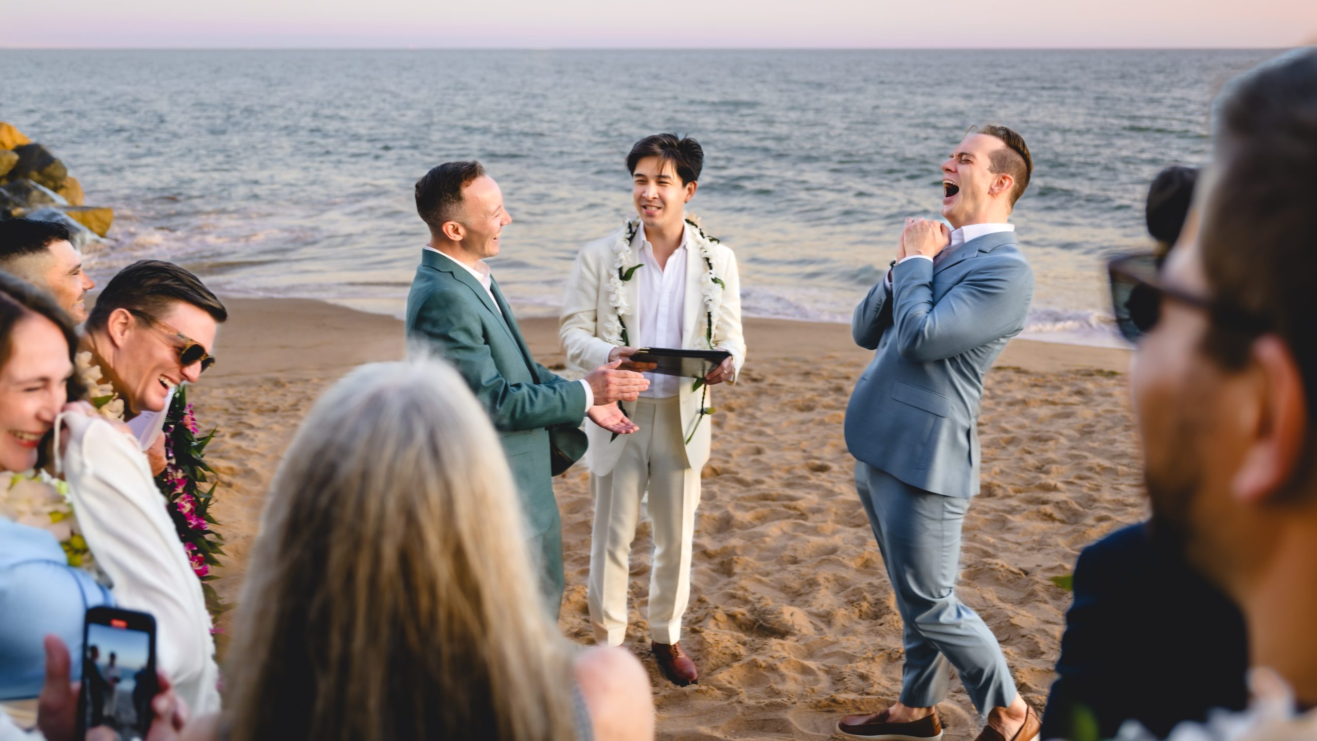 two grooms get married on a beach in malibu. They are laughing animatedly.